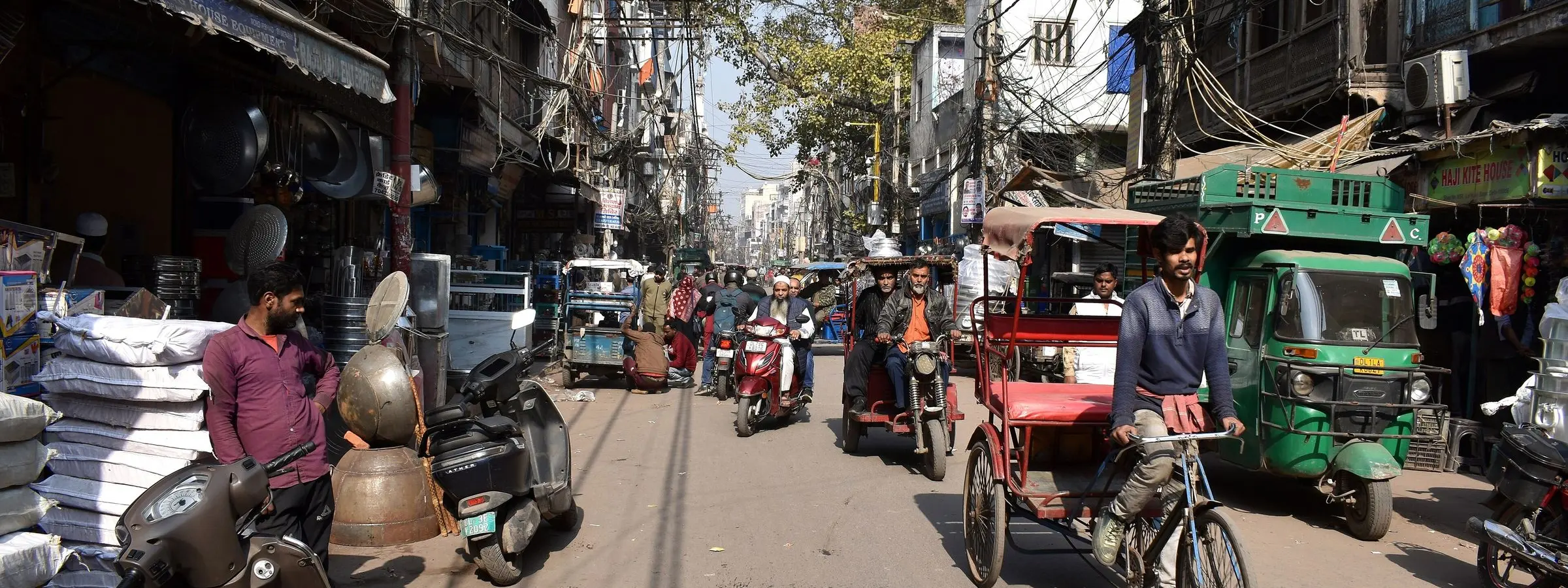 A busy bazaar lane in Old Delhi with cycle rickshaws, handcarts and sacks of goods outside the shops