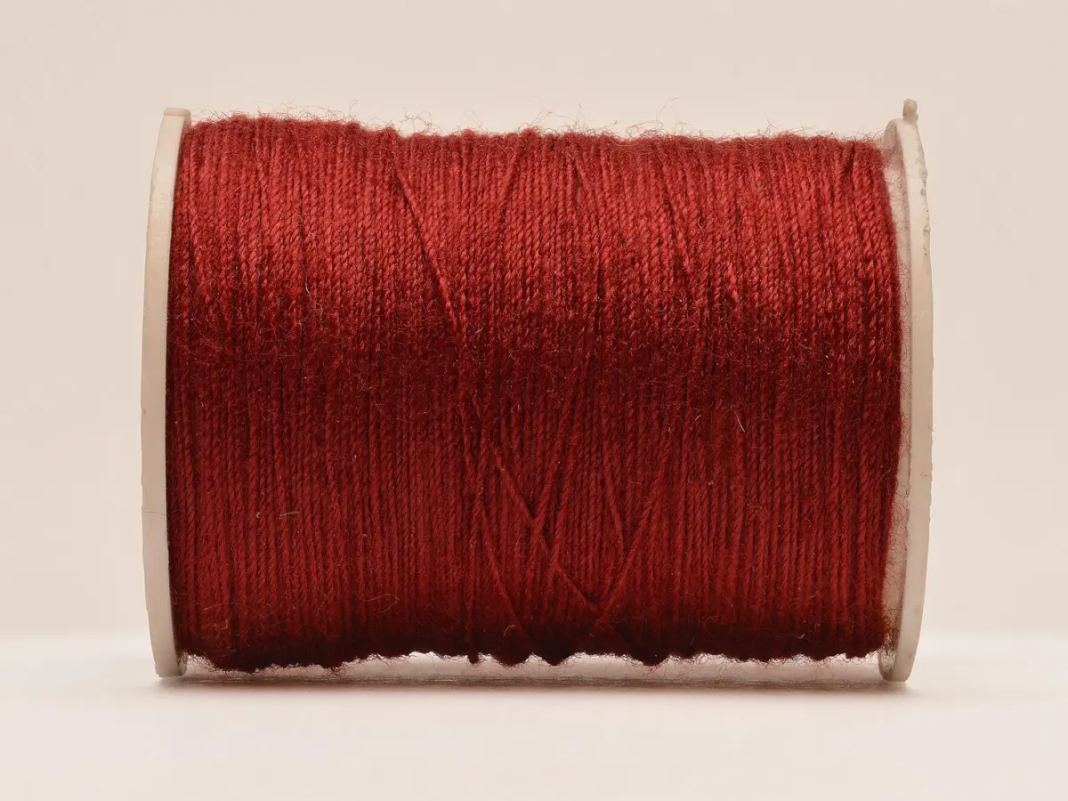 A full spool of red cotton thread standing on a plain pale ground