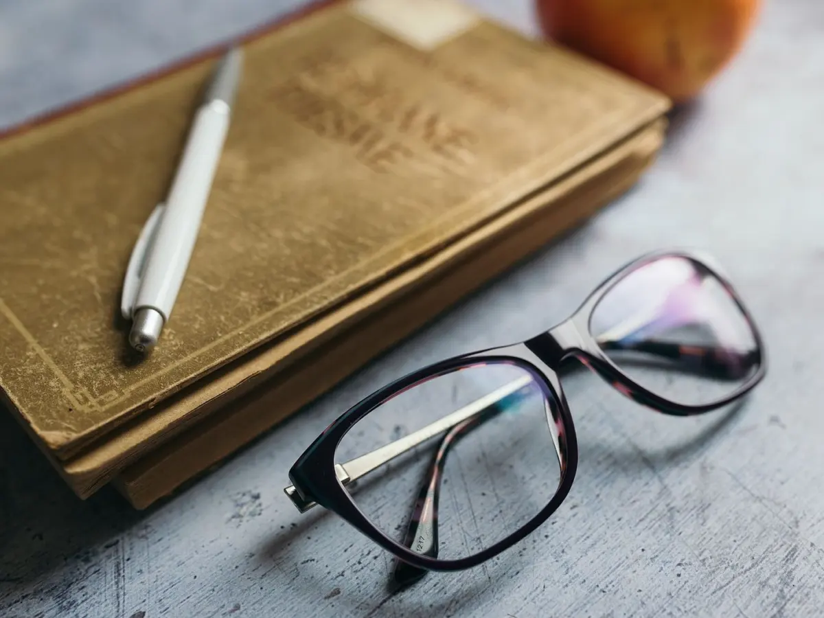A closed notebook with a pen and a pair of glasses resting on it