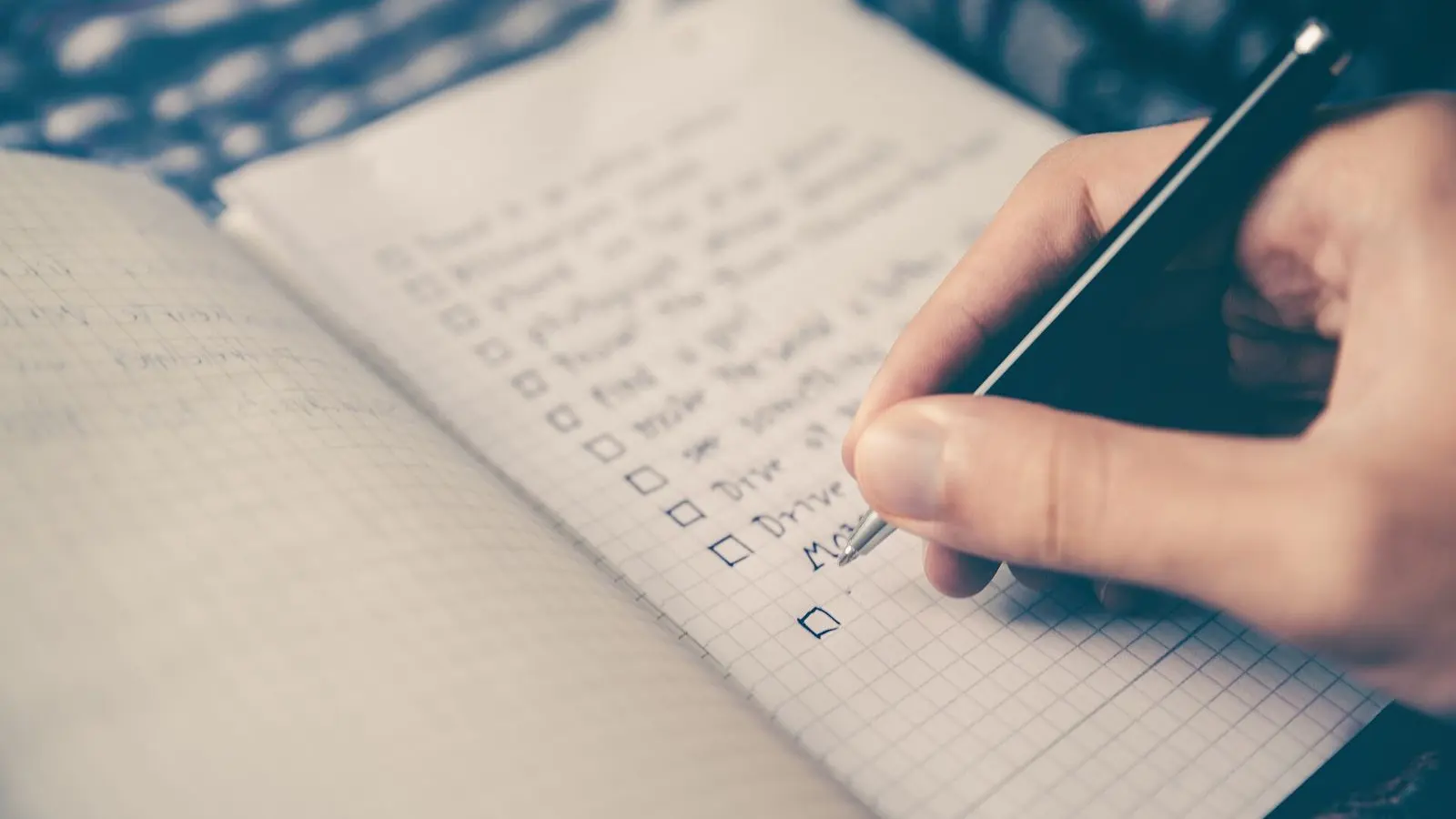 A hand writing a checklist with tick boxes in a squared notebook
