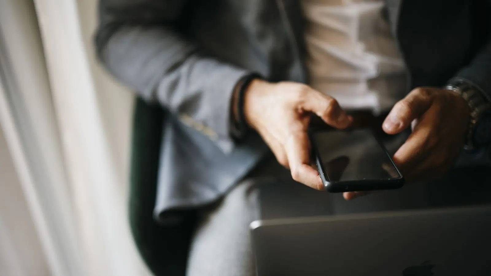 Hands holding a smartphone upright, the person seated and the screen turned away