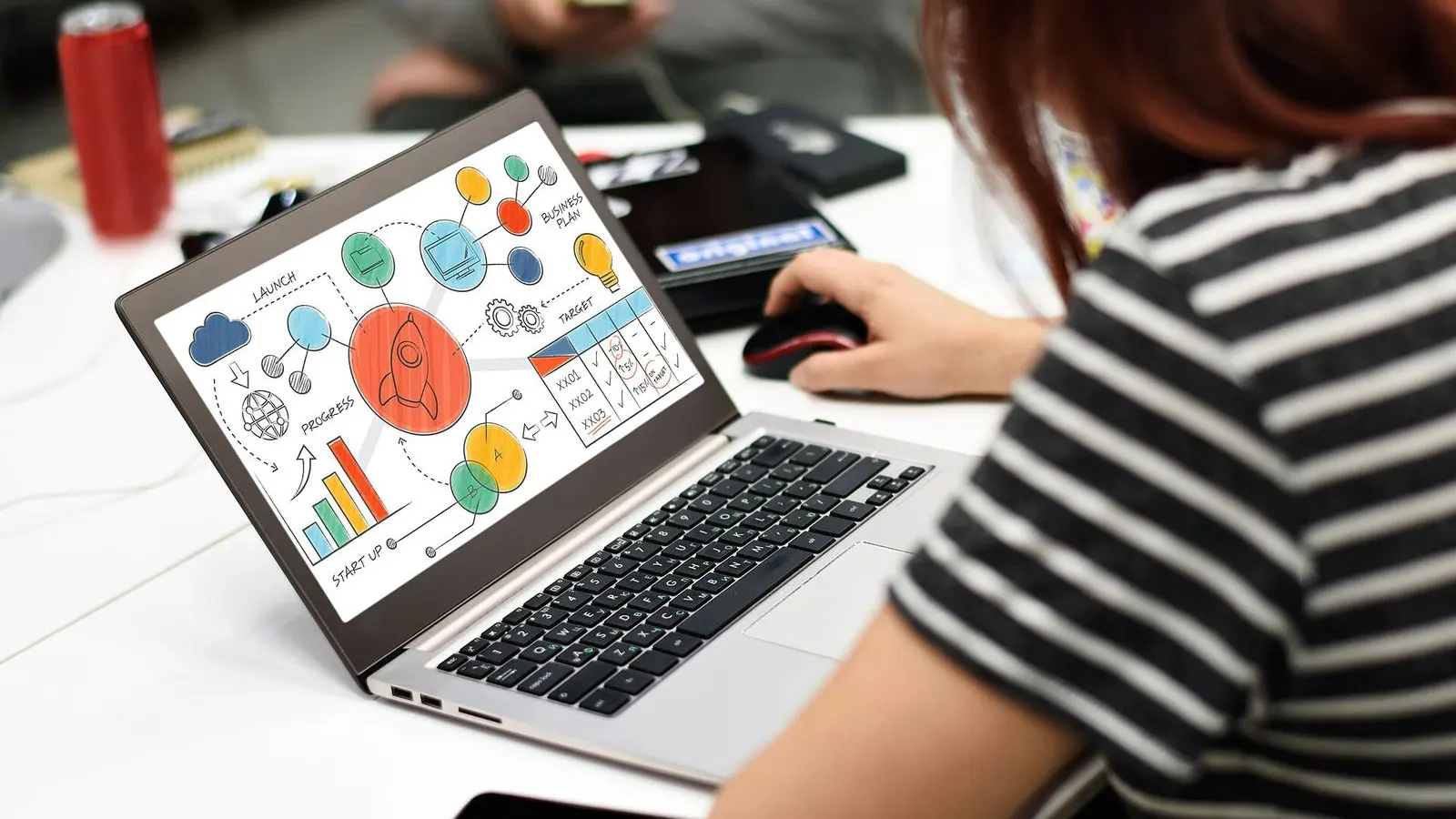 Hands on a laptop showing a colourful chart, on a white desk beside a cup