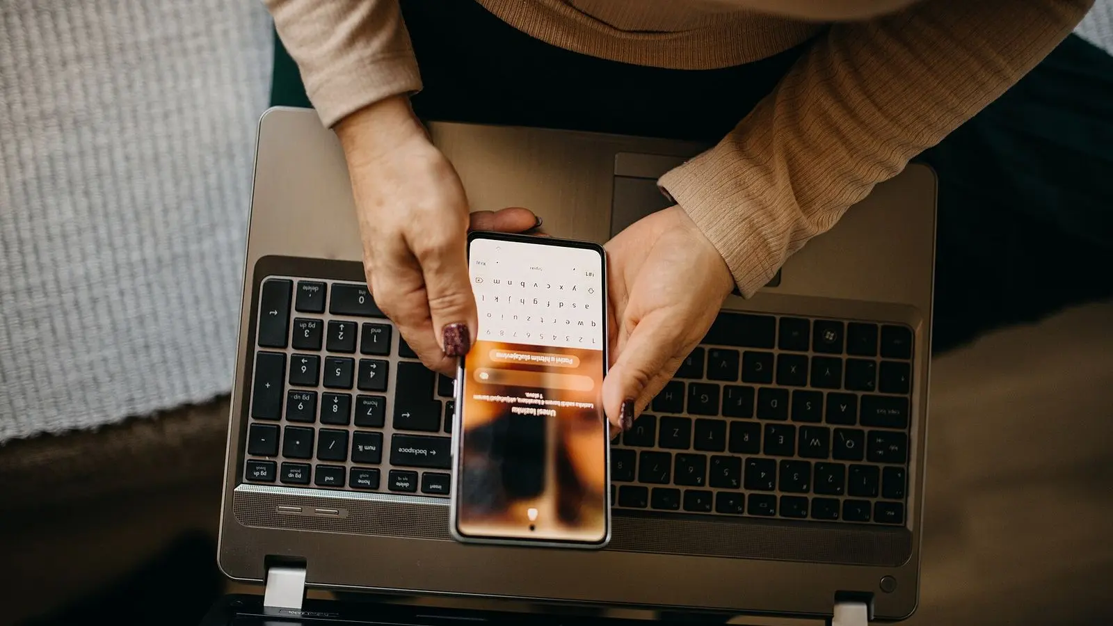 Hands holding a smartphone above an open laptop keyboard