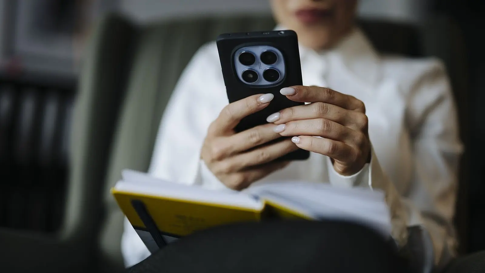 A seated person holding a smartphone in both hands, a notebook open on their lap