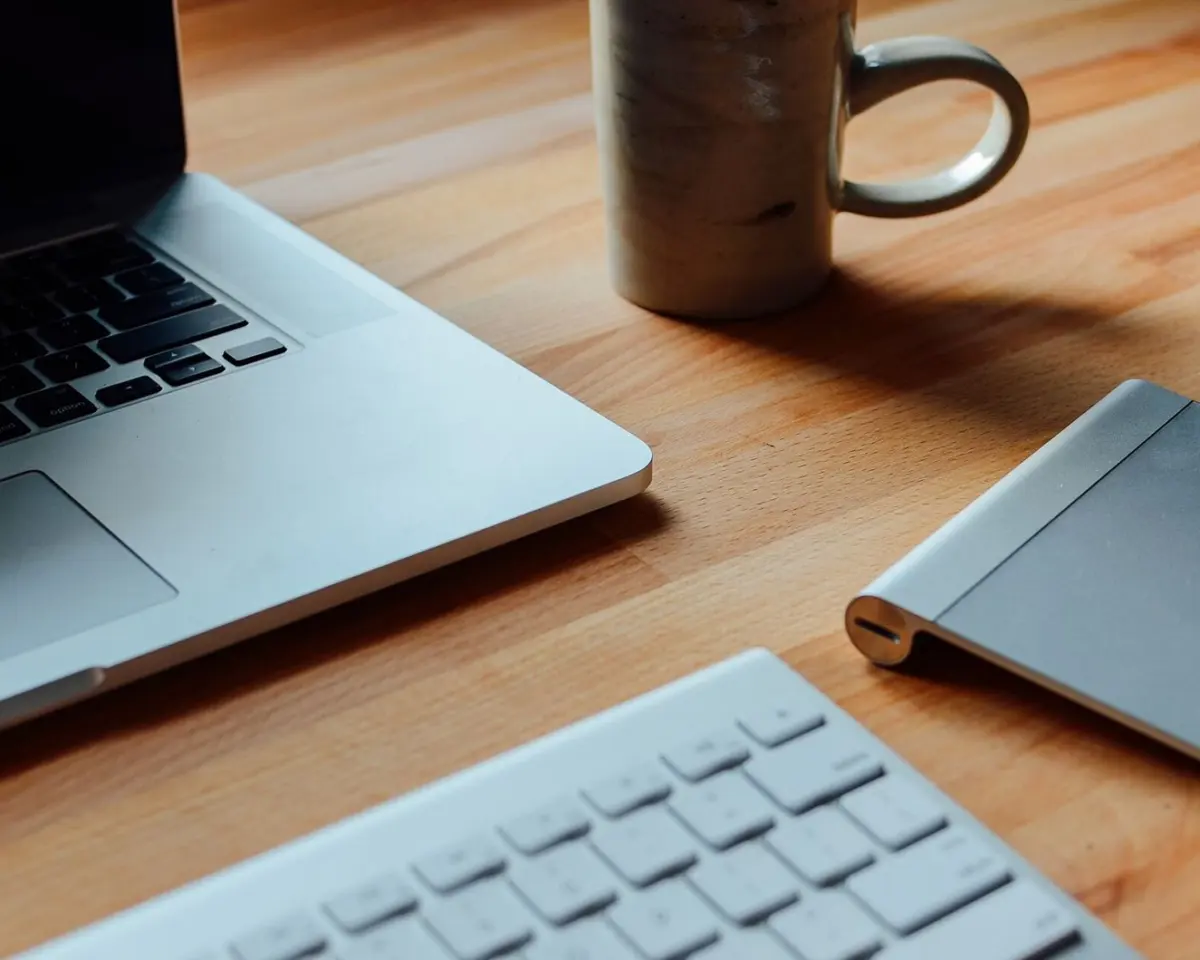 A laptop and a mug on a light wooden desk, seen from above
