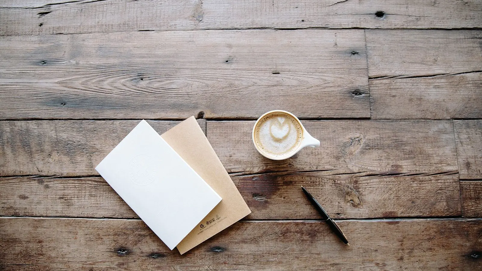 Notebooks, a pen and a cup of coffee on a weathered wooden table