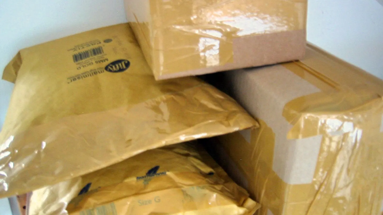 A pile of padded mailing envelopes and a taped cardboard parcel, seen close