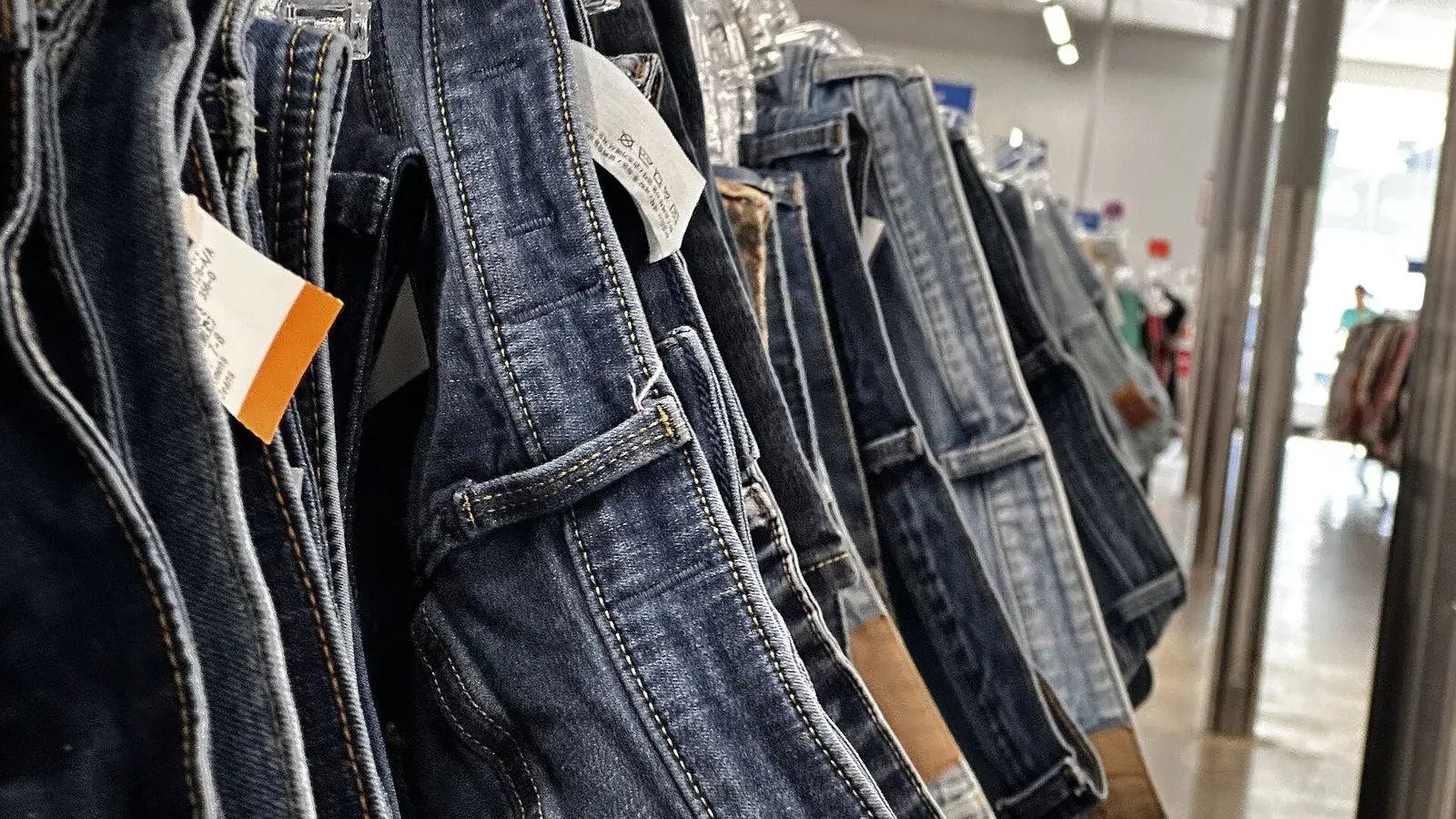 Jeans hung close together on a rack in a clothing store, a care label and a price tag showing