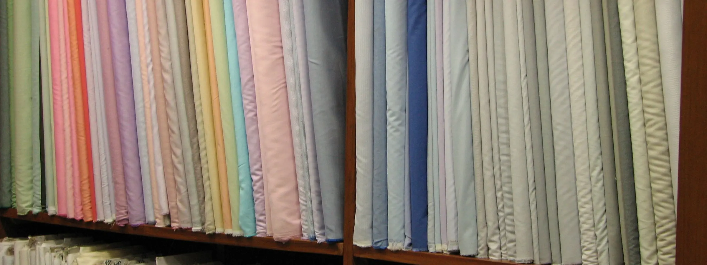 Shelves stacked with folded suiting fabric in rows of colour inside a cloth shop in India