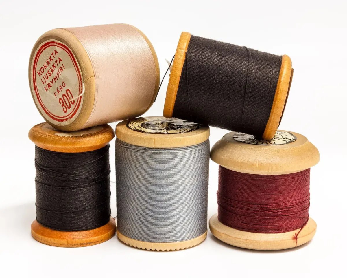 Wooden spools of sewing thread in red, grey, black and cream stacked on one another