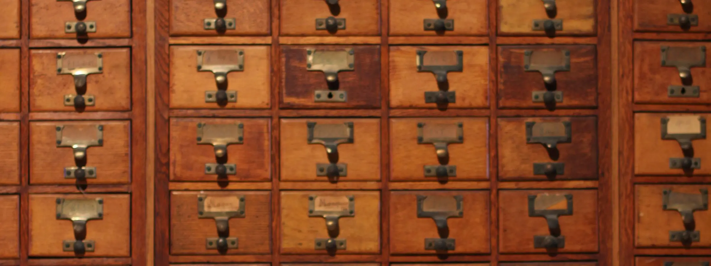 Rows of small wooden index drawers with brass label holders in an old filing cabinet