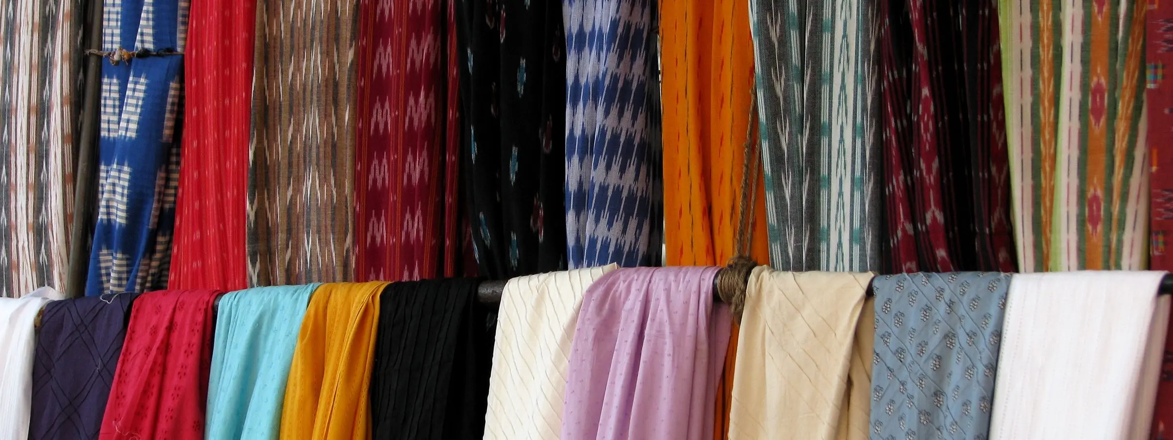 Bolts of cloth in many colours stacked on the shelves of a fabric shop in Chennai