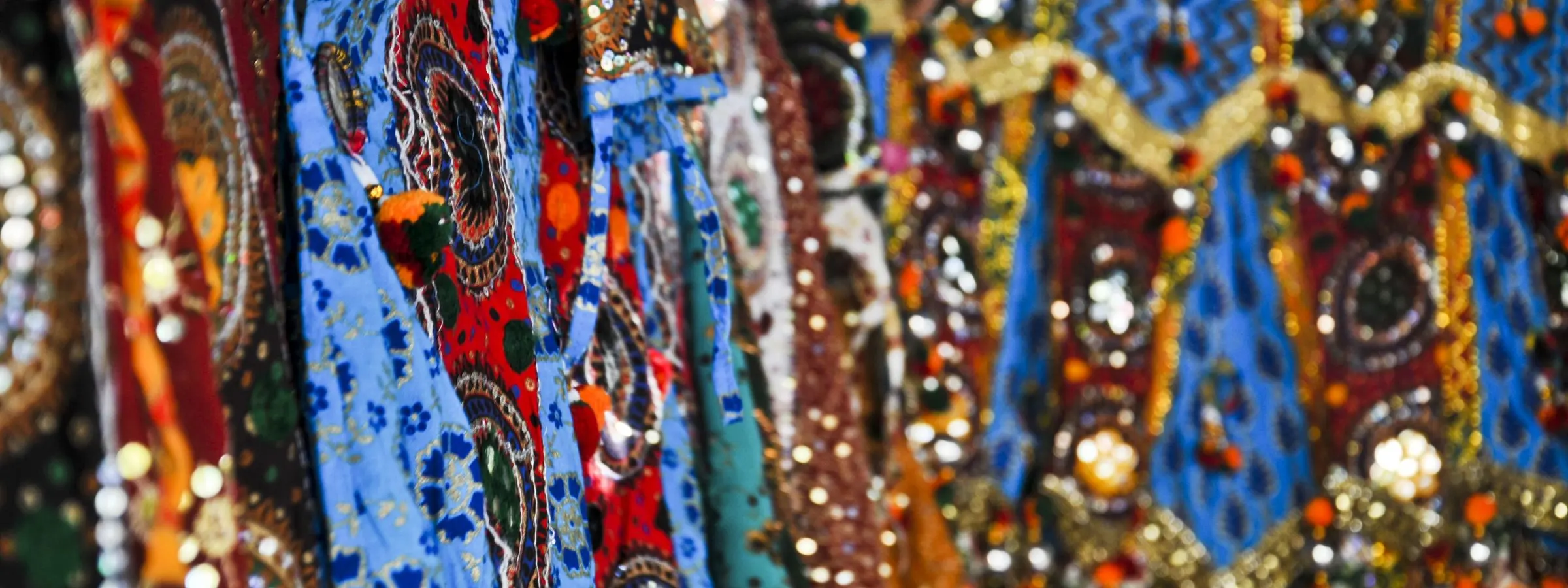 Mirror-work and embroidered chaniya cholis in blue, red and gold hanging close together at Law Garden, Ahmedabad