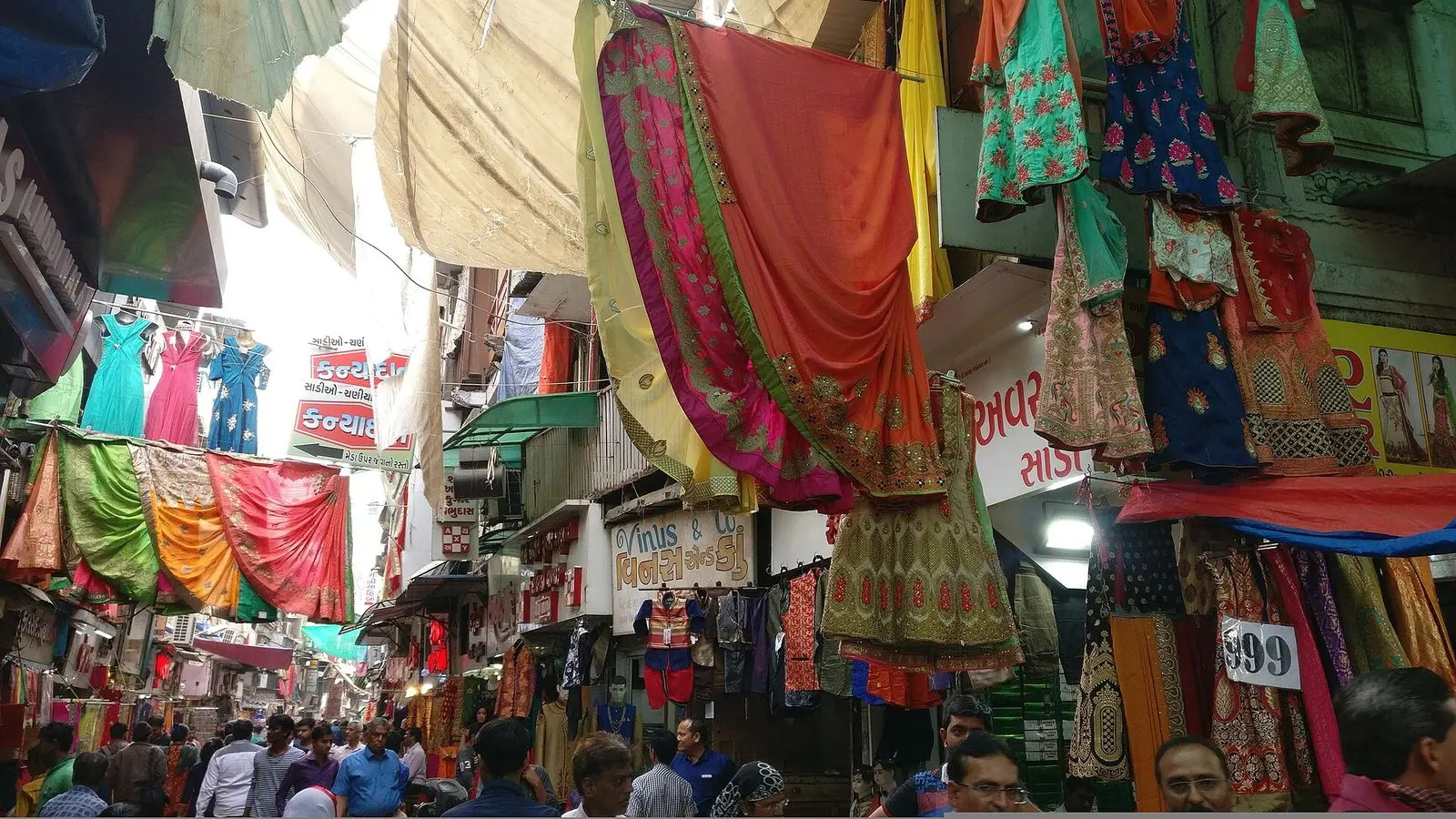 Sarees and printed fabrics hanging above sari sellers' shops along a street in Ratan Pol, Ahmedabad