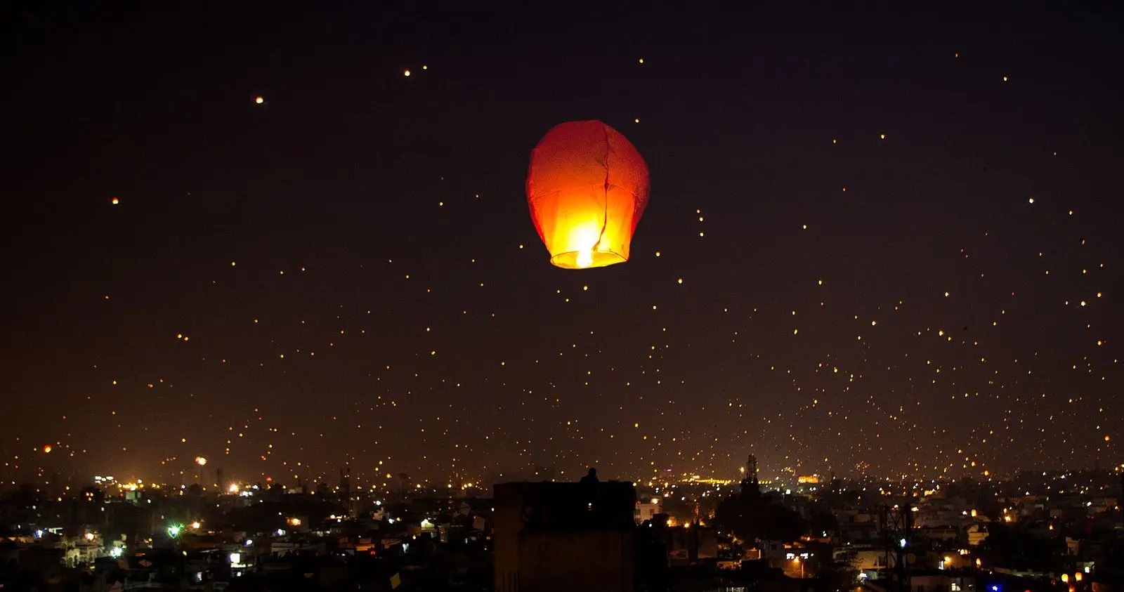 A glowing paper sky lantern rising over city lights on the night of Uttarayan