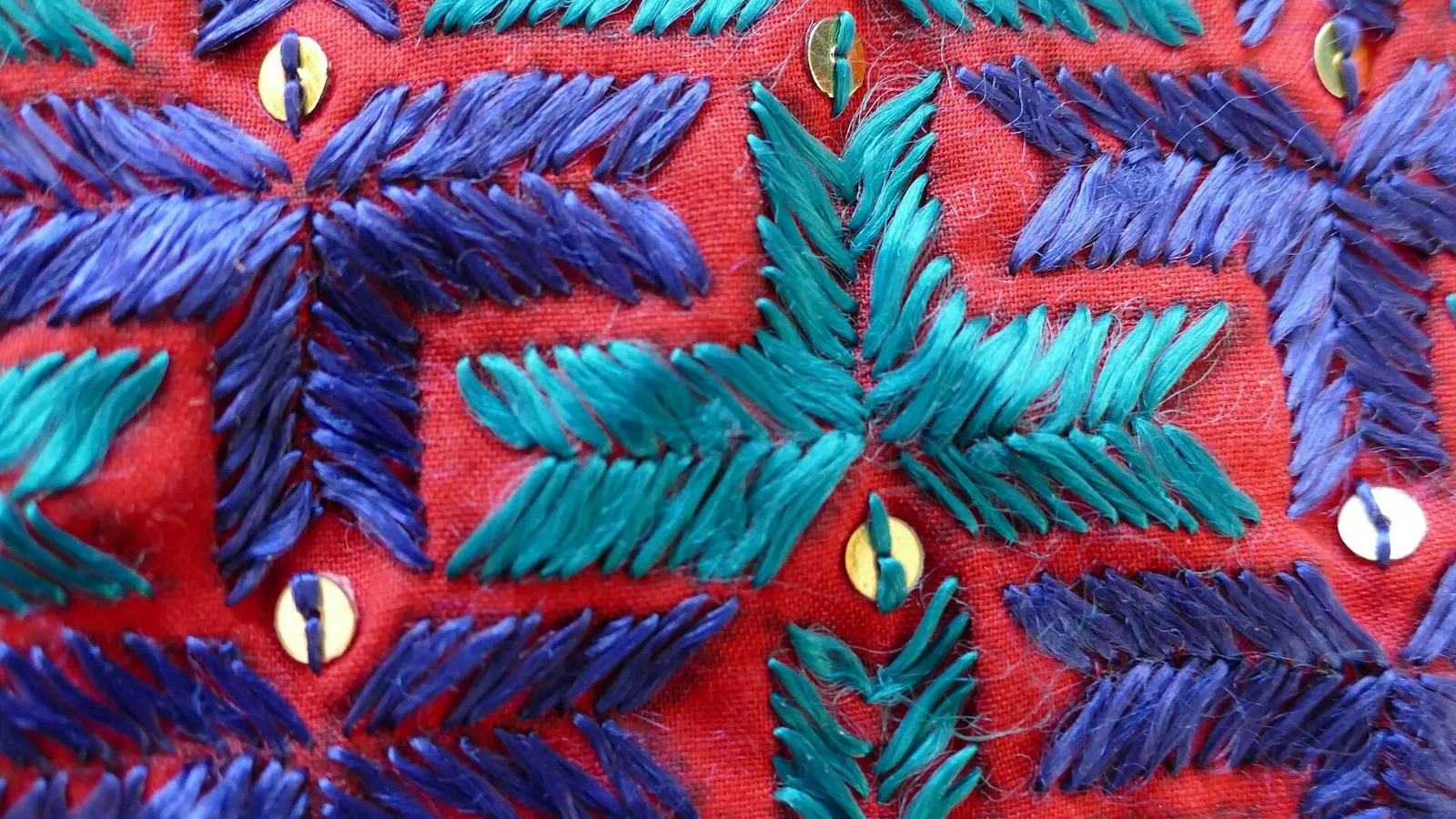 Close view of a shawl from Punjab embroidered in violet, teal and blue on red, with sequins