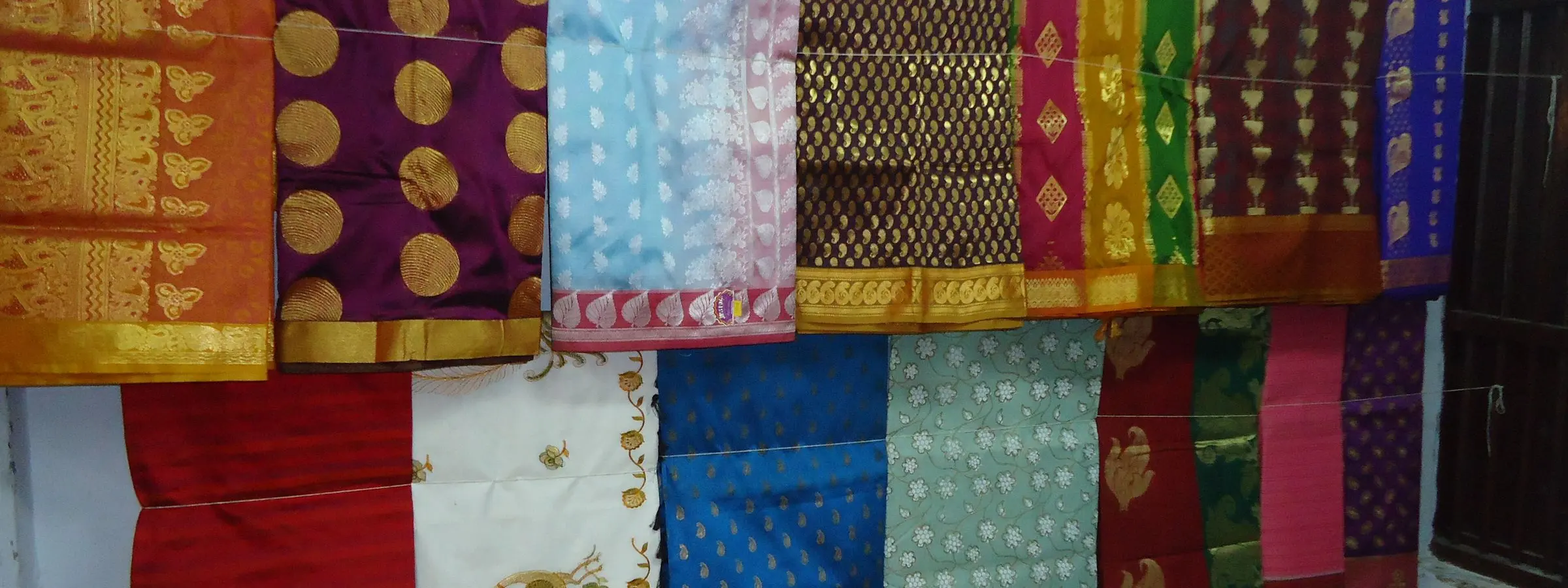 Kanchipuram silk sarees with contrasting zari borders hung in rows for sale in a Kanchipuram shop
