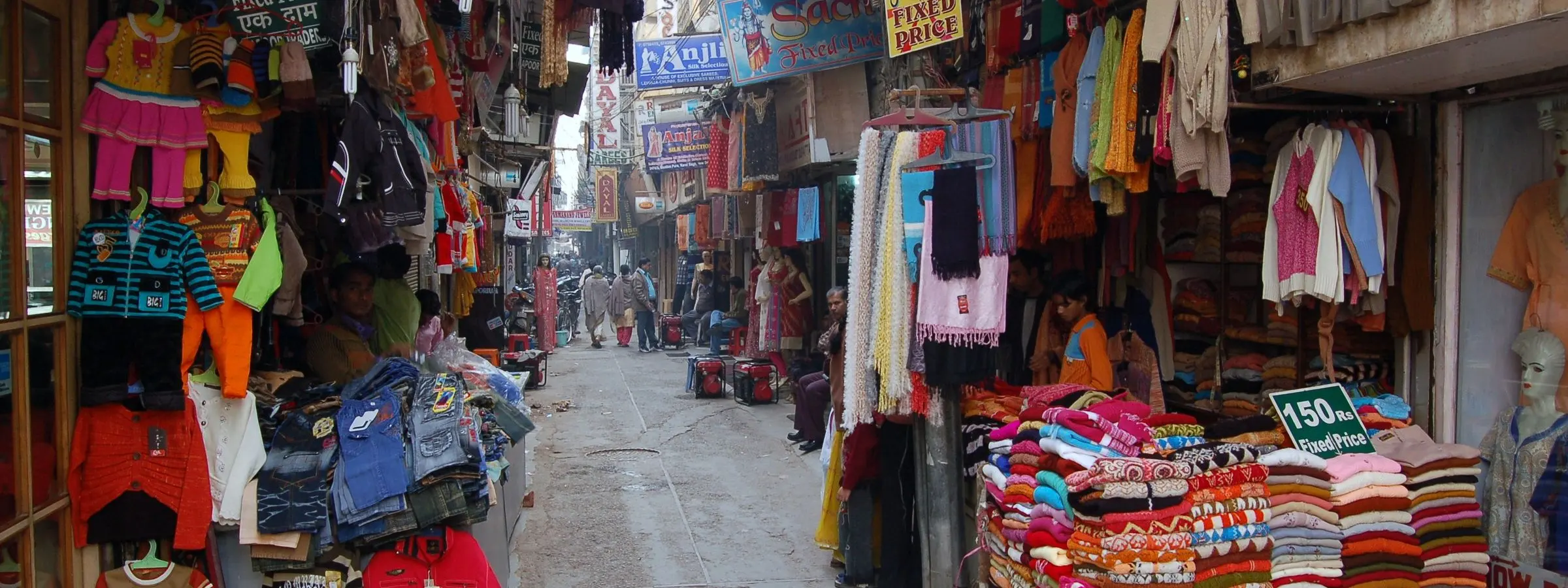 Shopfronts in a Karol Bagh market lane stacked with folded readymade garments and hanging clothes, Delhi
