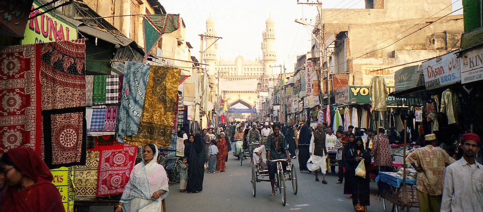 Printed fabrics hanging from shopfronts along a busy bazaar street near Charminar, Hyderabad