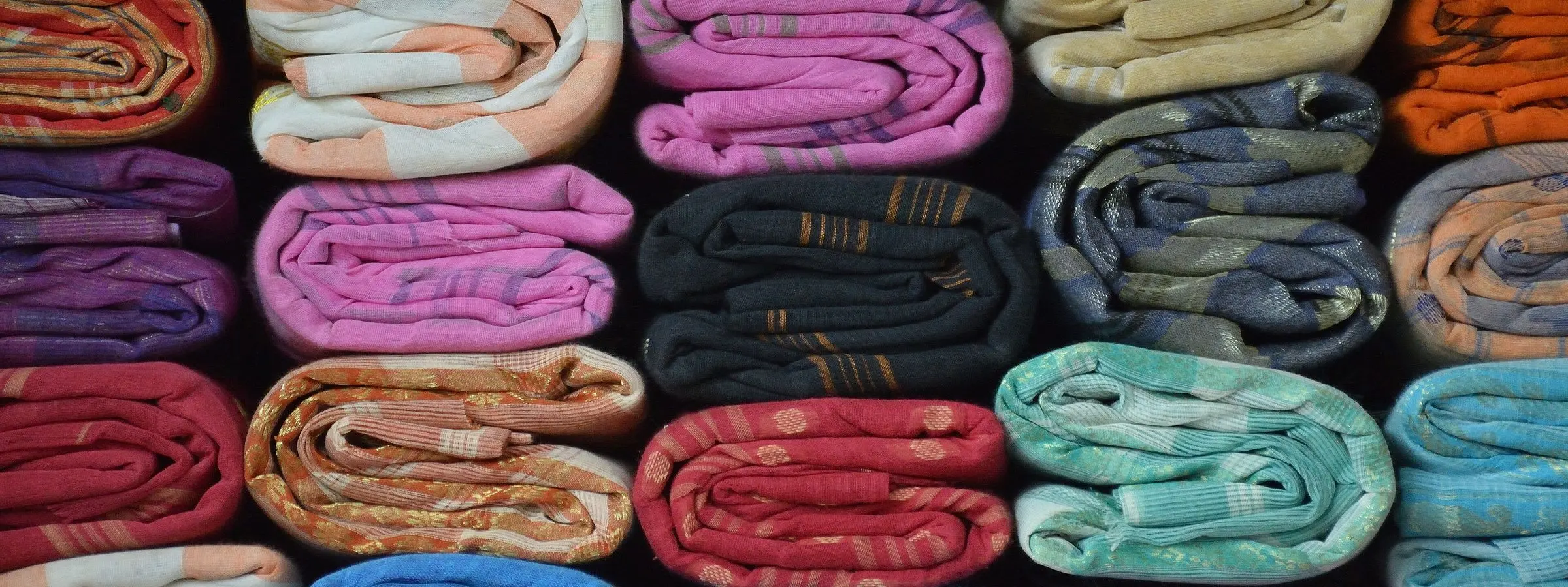 Tant sarees in bright colours folded and stacked on shelves at a handloom centre in Phulia, Nadia