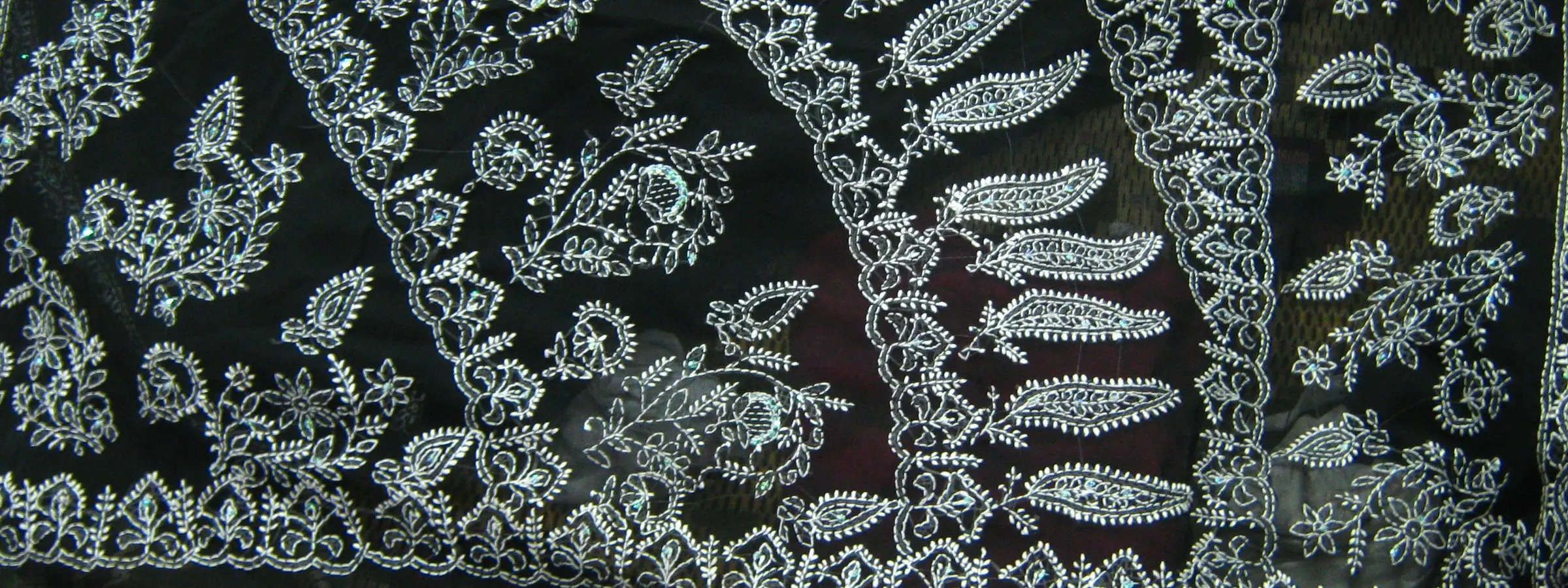 White chikan embroidery of leaves, paisleys and flowers worked across the dark pallu of a saree