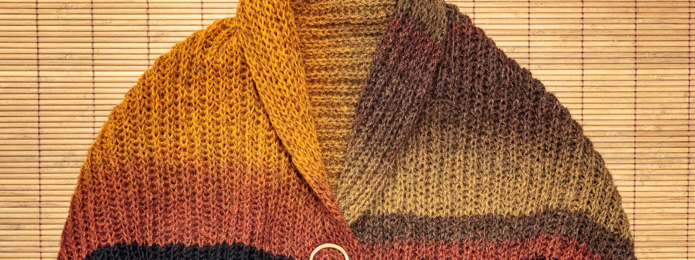 A hand-knitted shawl in fisherman's rib, shading from mustard and rust to black, fastened with a brooch