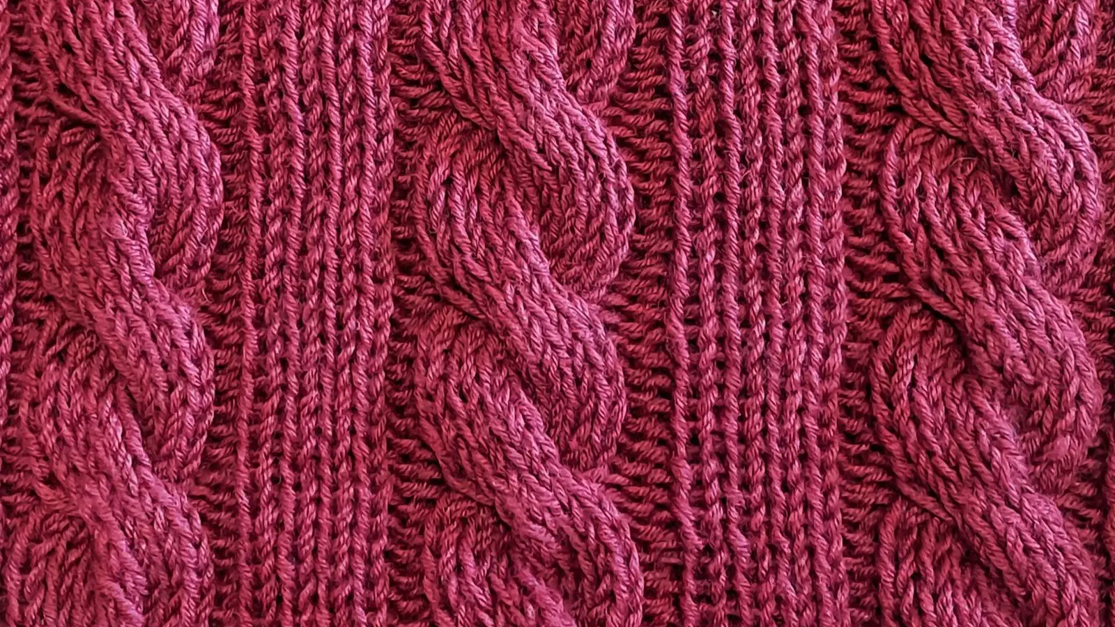 Close view of cable and rib stitches on a hand-knitted sweater in deep rose wool