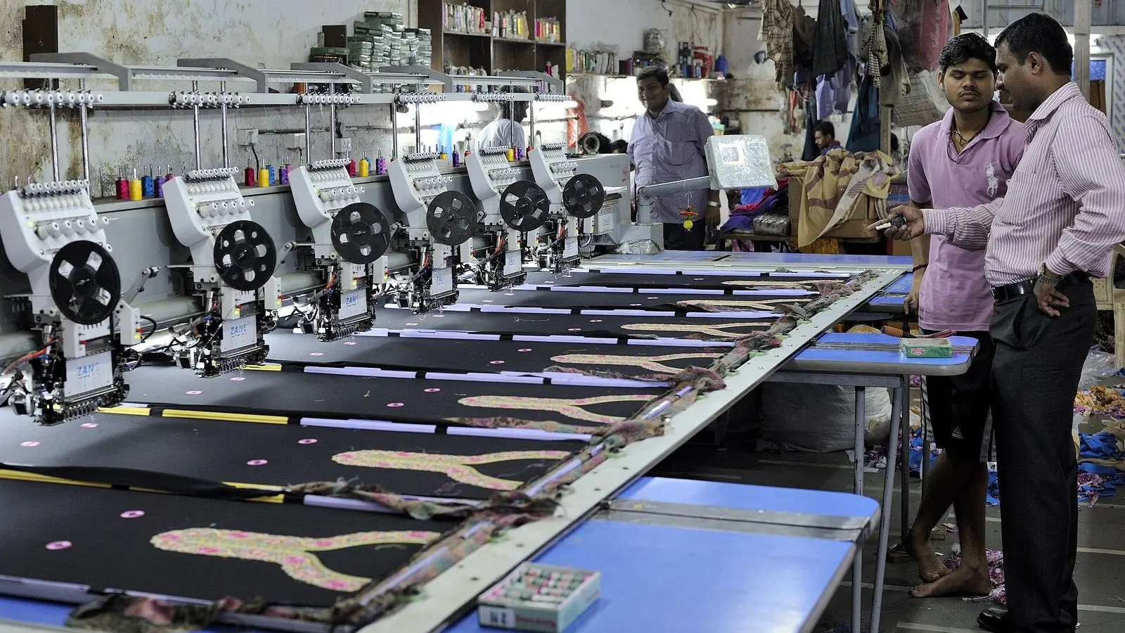 Rows of multi-head embroidery machines stitching fabric panels in a workshop in Dharavi, Mumbai