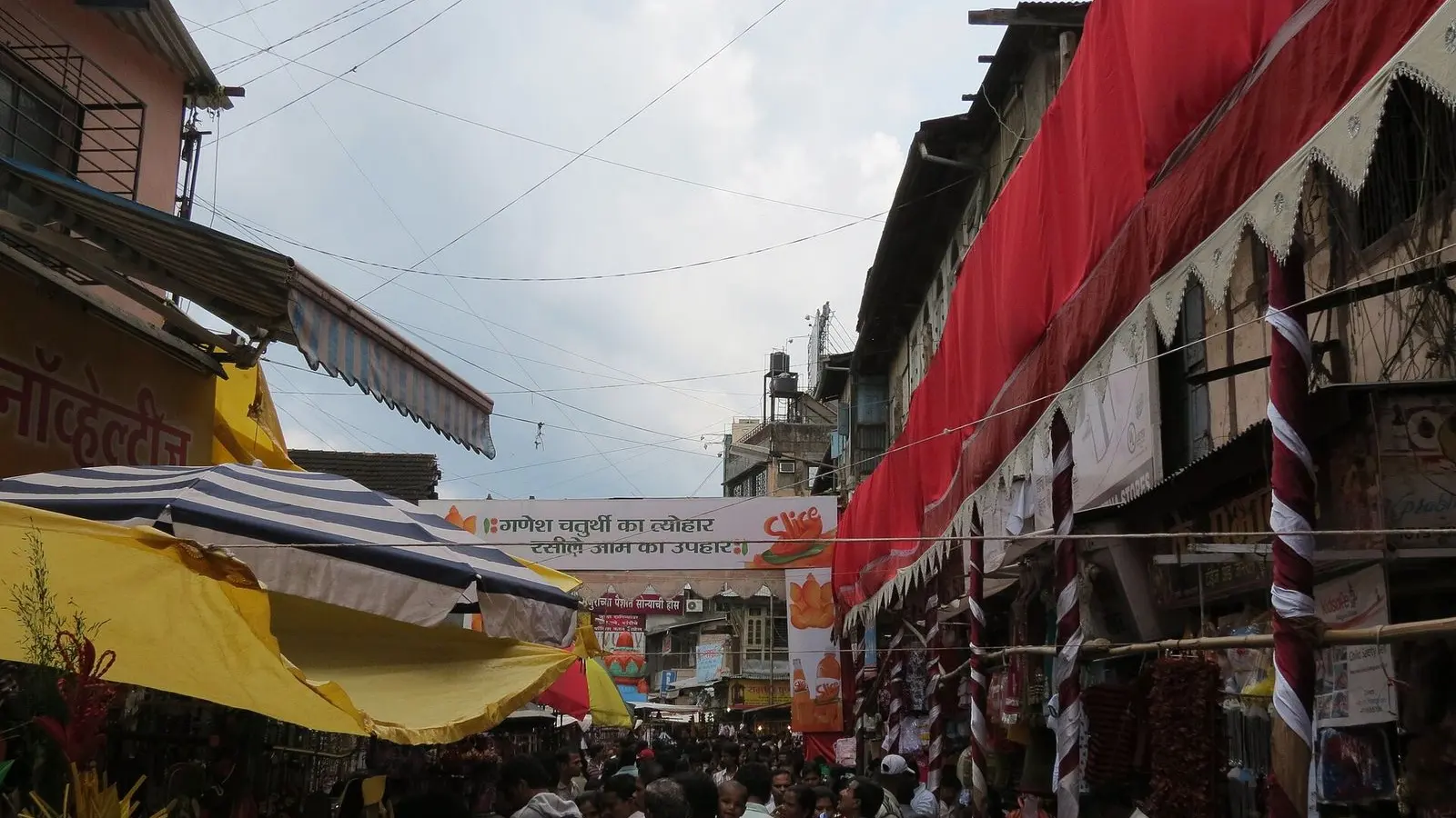 Shoppers crowding a market street under red awnings in central Pune during Ganesh Chaturthi