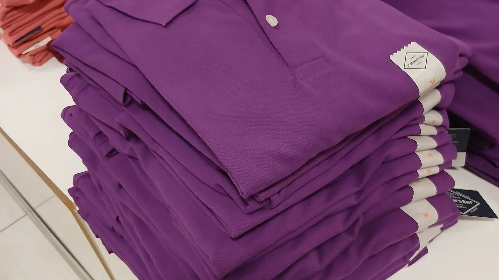 A tall stack of folded purple polo shirts on a store table, peach polos beside it