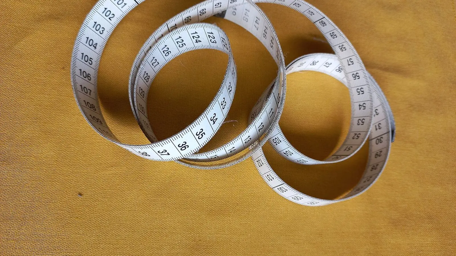 A coiled cloth measuring tape lying loose on a mustard-yellow fabric