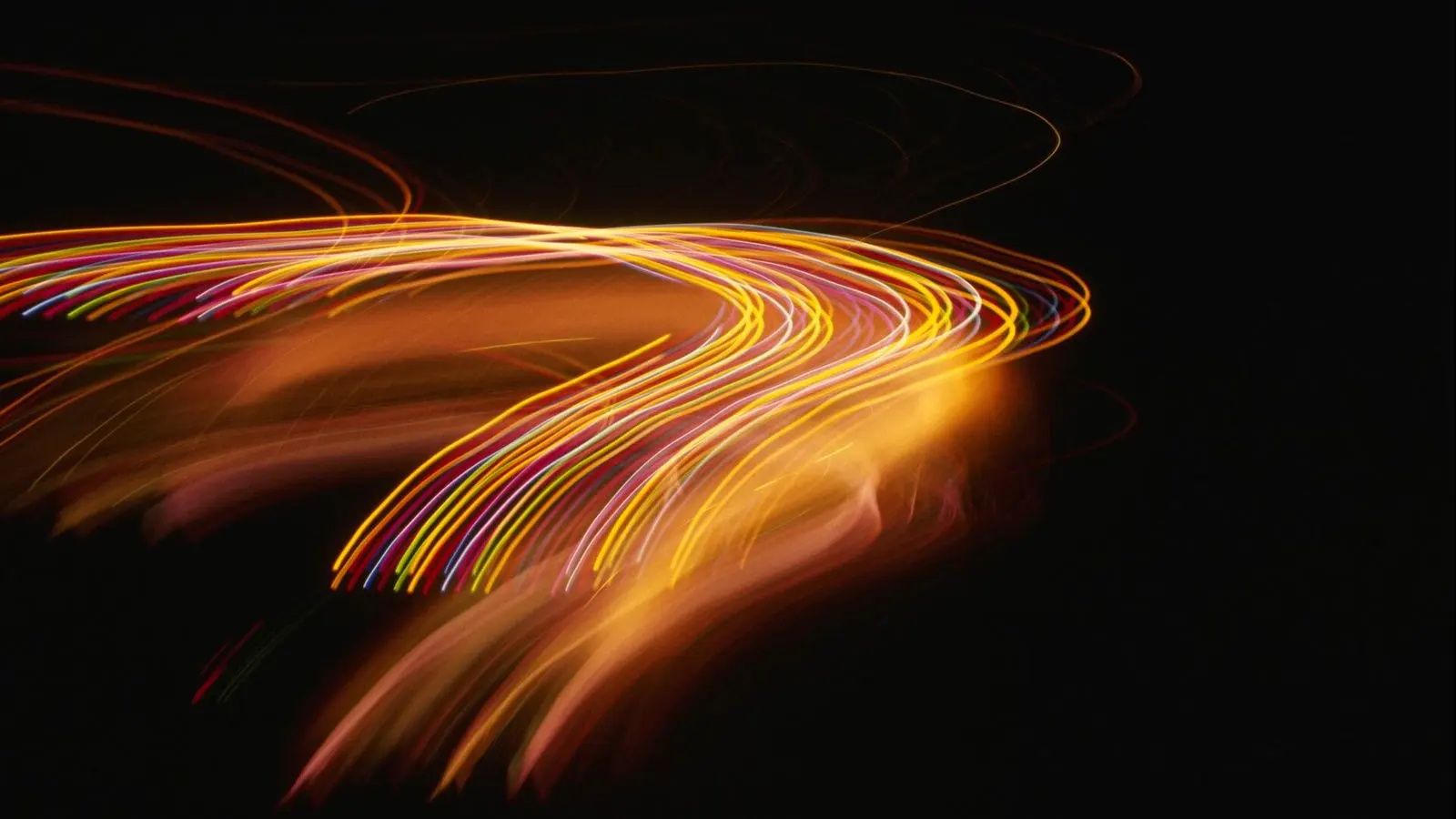 Curved trails of orange and gold light on a black background, drawn by a long camera exposure