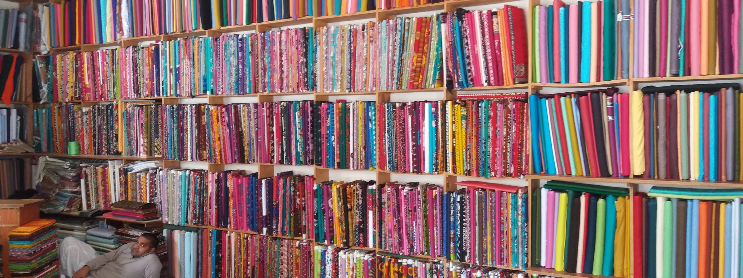 Bolts of cloth in many colours stacked floor to ceiling on a shop's shelves