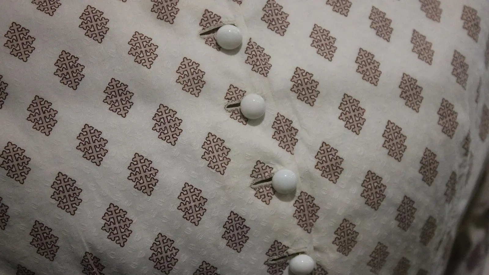A close view of a printed cotton garment, a small red motif repeated across cream cloth, with white buttons