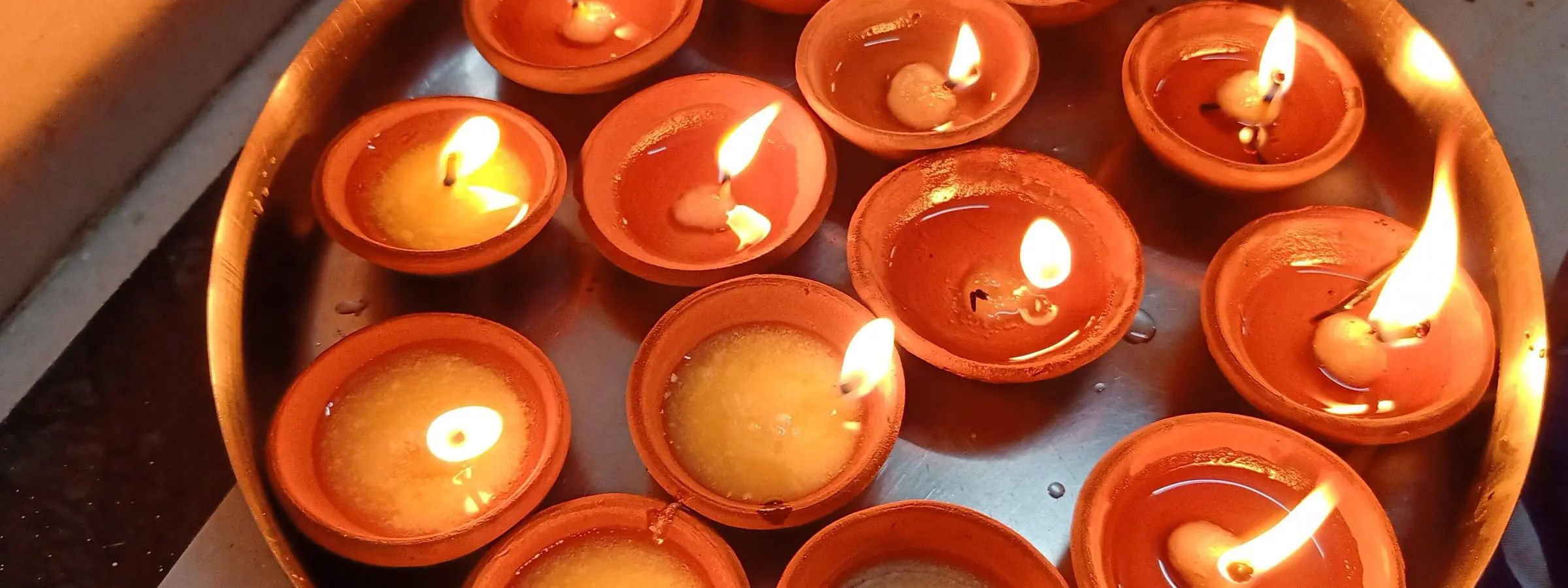 Lit clay diyas arranged on a round brass plate, their flames glowing in low light