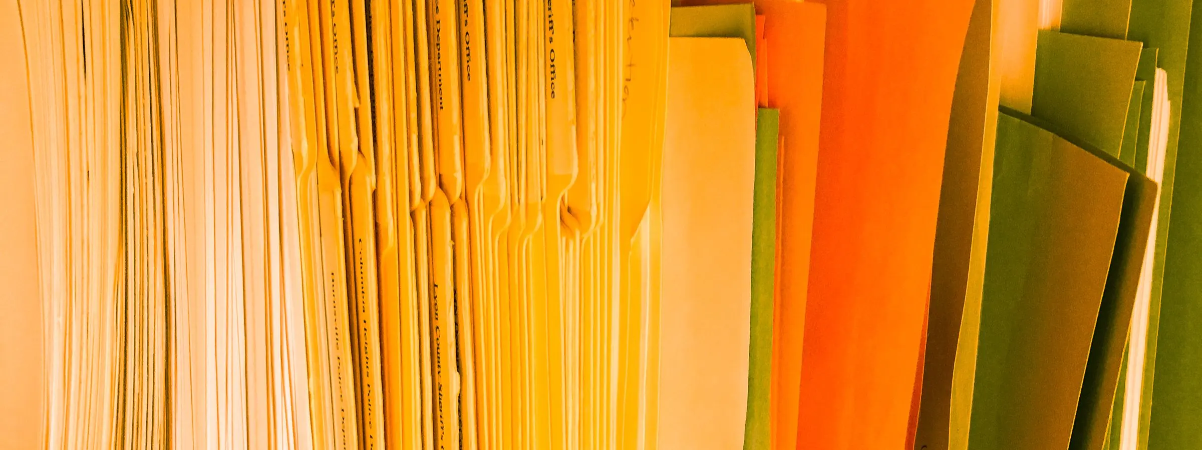 Rows of yellow, orange and green paper document folders packed upright on a shelf