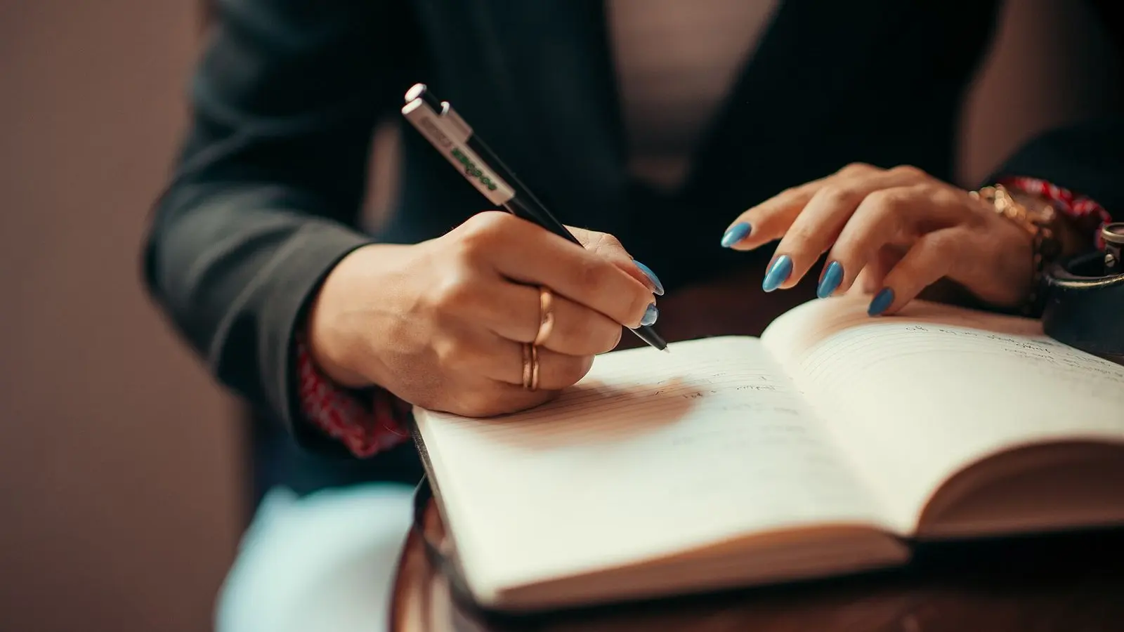 Hands writing with a pen in an open notebook on a dark table