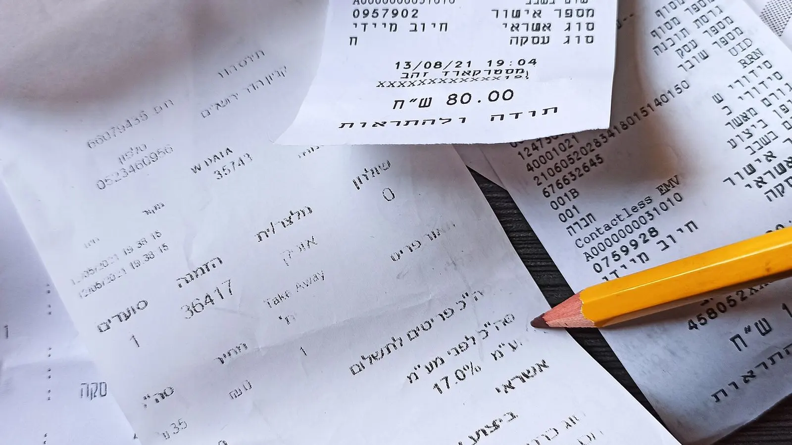Printed bills and receipts piled on a white table with a pencil resting across them