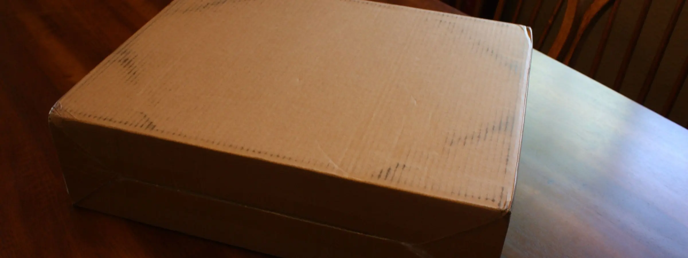 A plain closed cardboard box on a dark wooden table in warm indoor light