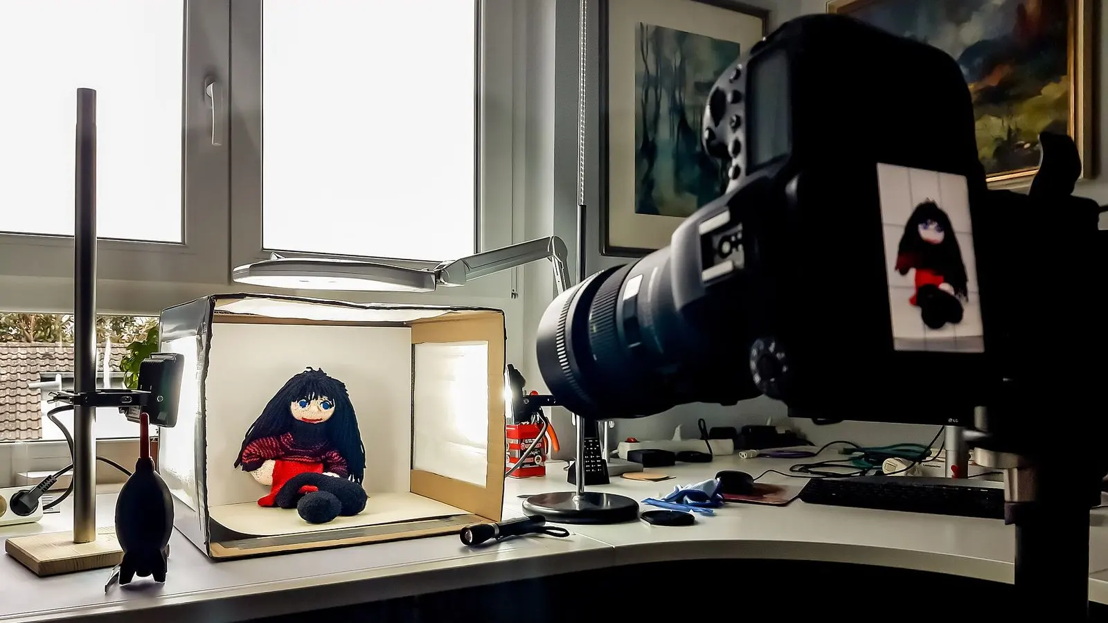 A camera on a stand photographing a small soft toy inside a white light tent on a desk