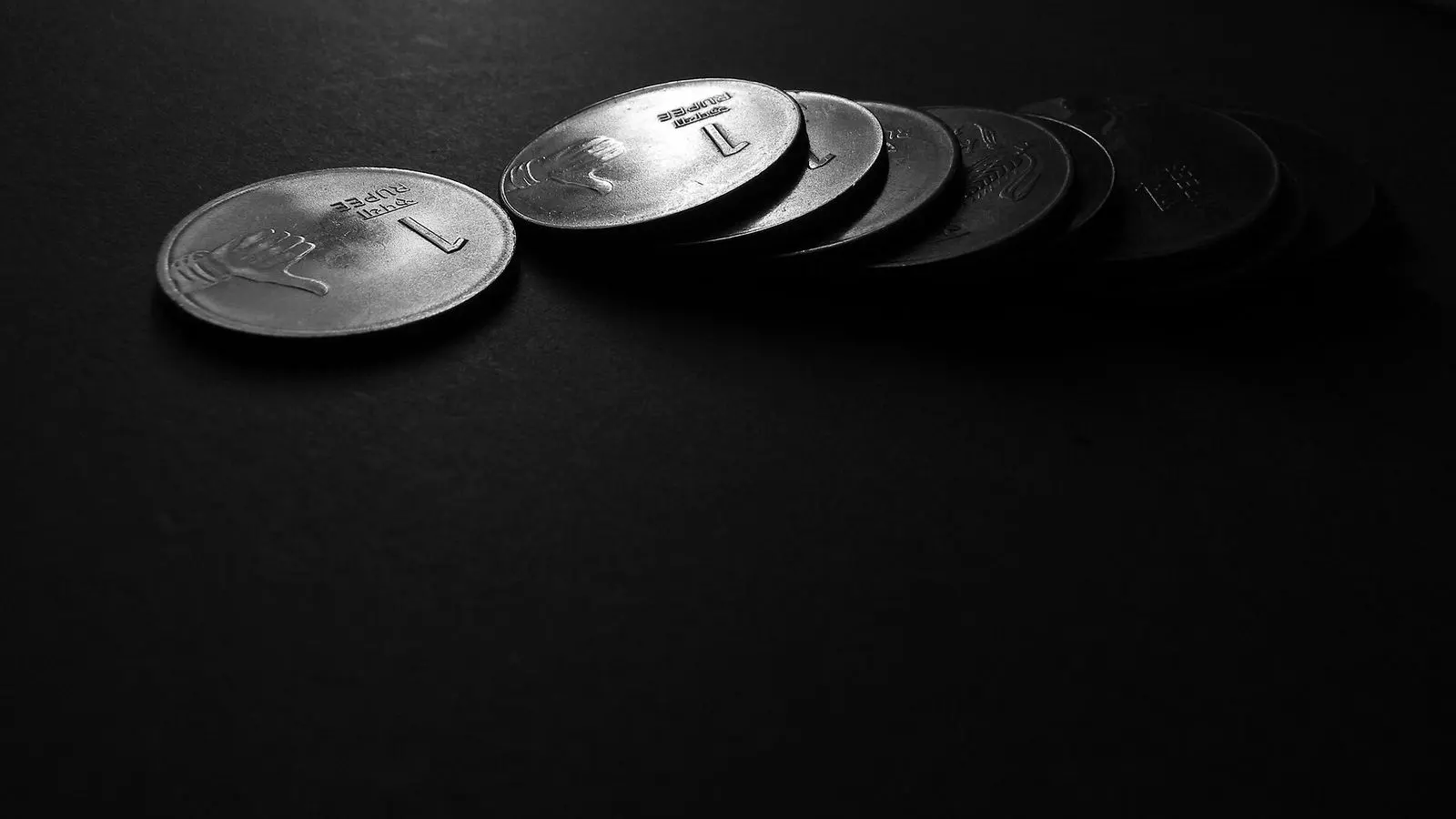 Indian one rupee coins laid in an overlapping row on a dark surface, lit from the side