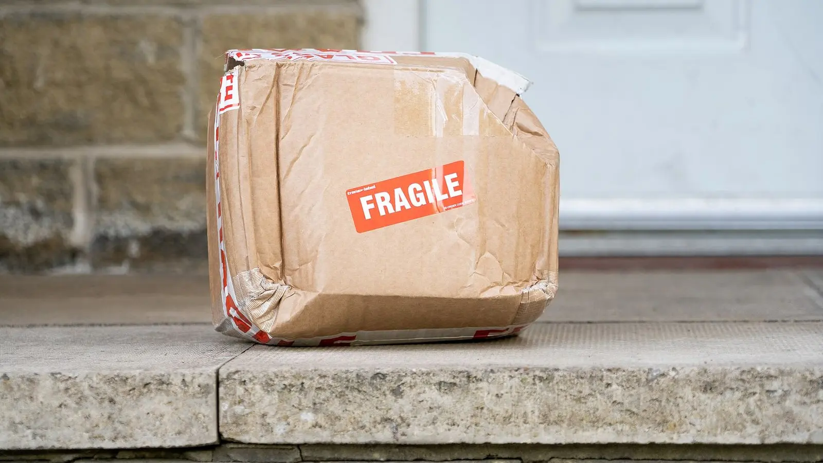 A crushed cardboard parcel with a red fragile sticker, left on a stone doorstep