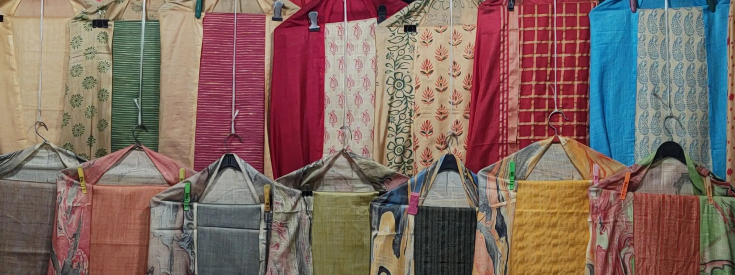 Lengths of printed kurti cloth in red, saffron, cream and blue hanging in rows at a shop