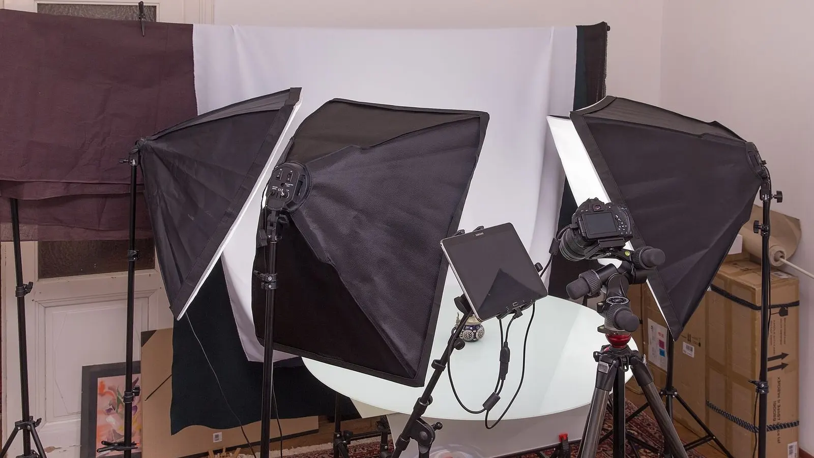 A product photography studio with two softbox lights on stands around a white shooting table