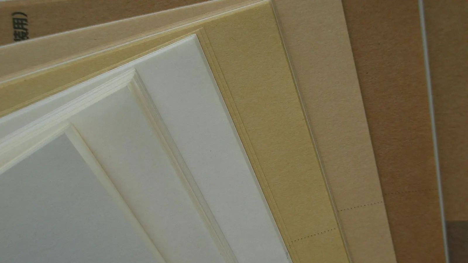 Sheets of cream and tan packaging paper and card fanned out in layers