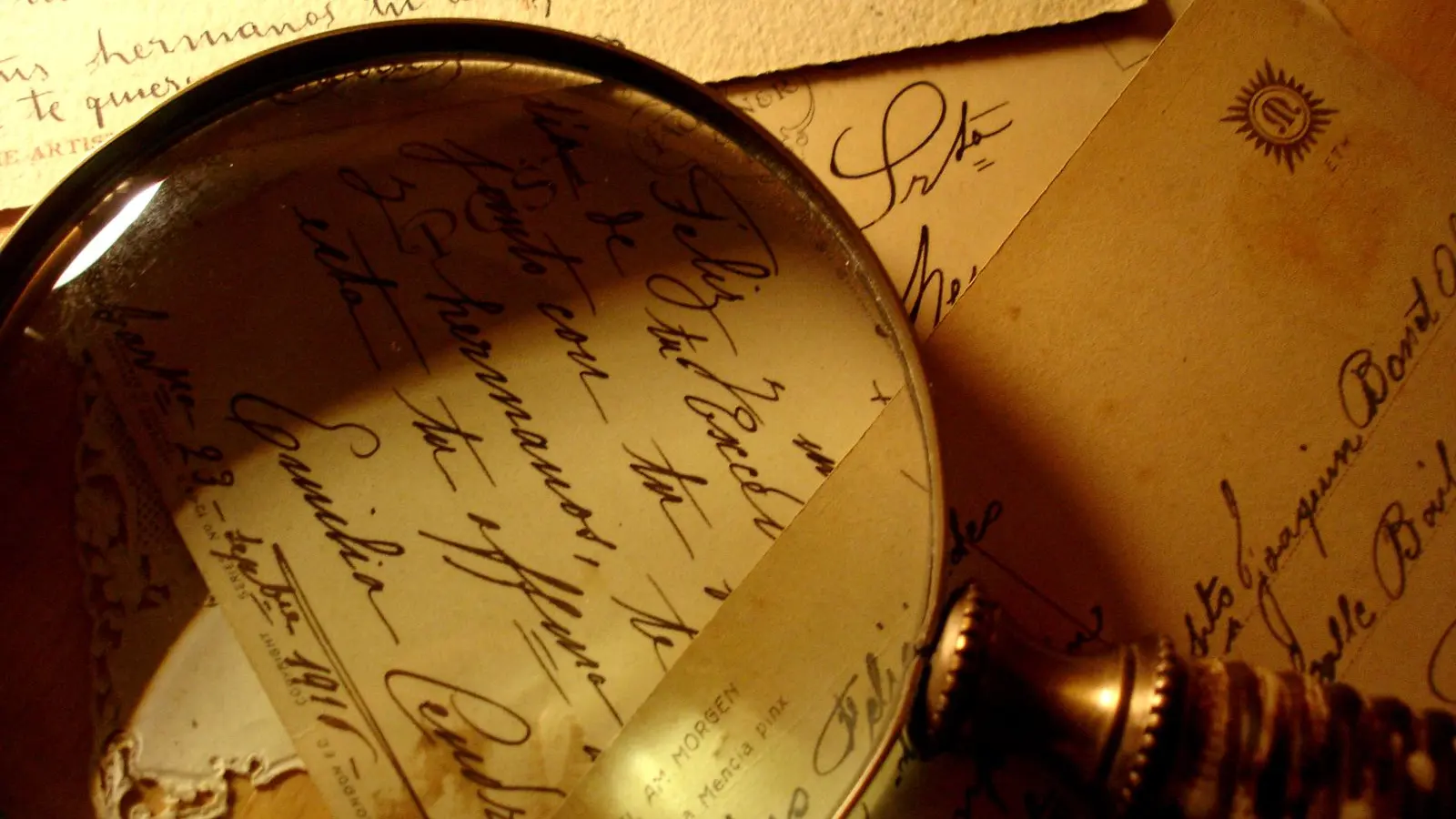 A magnifying glass resting on old handwritten postcards in warm golden light