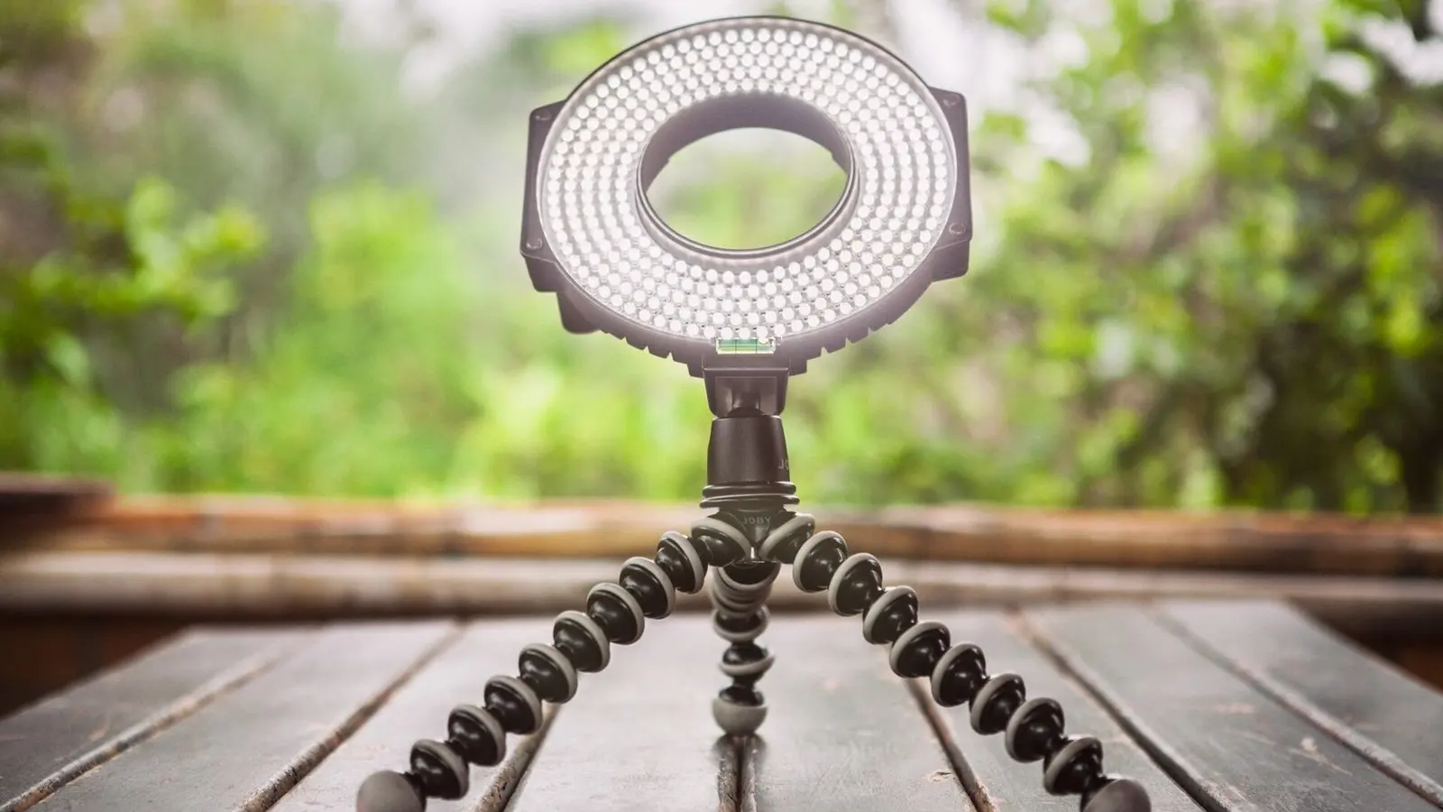 An LED ring light on a small flexible tripod standing on a weathered wooden table outdoors