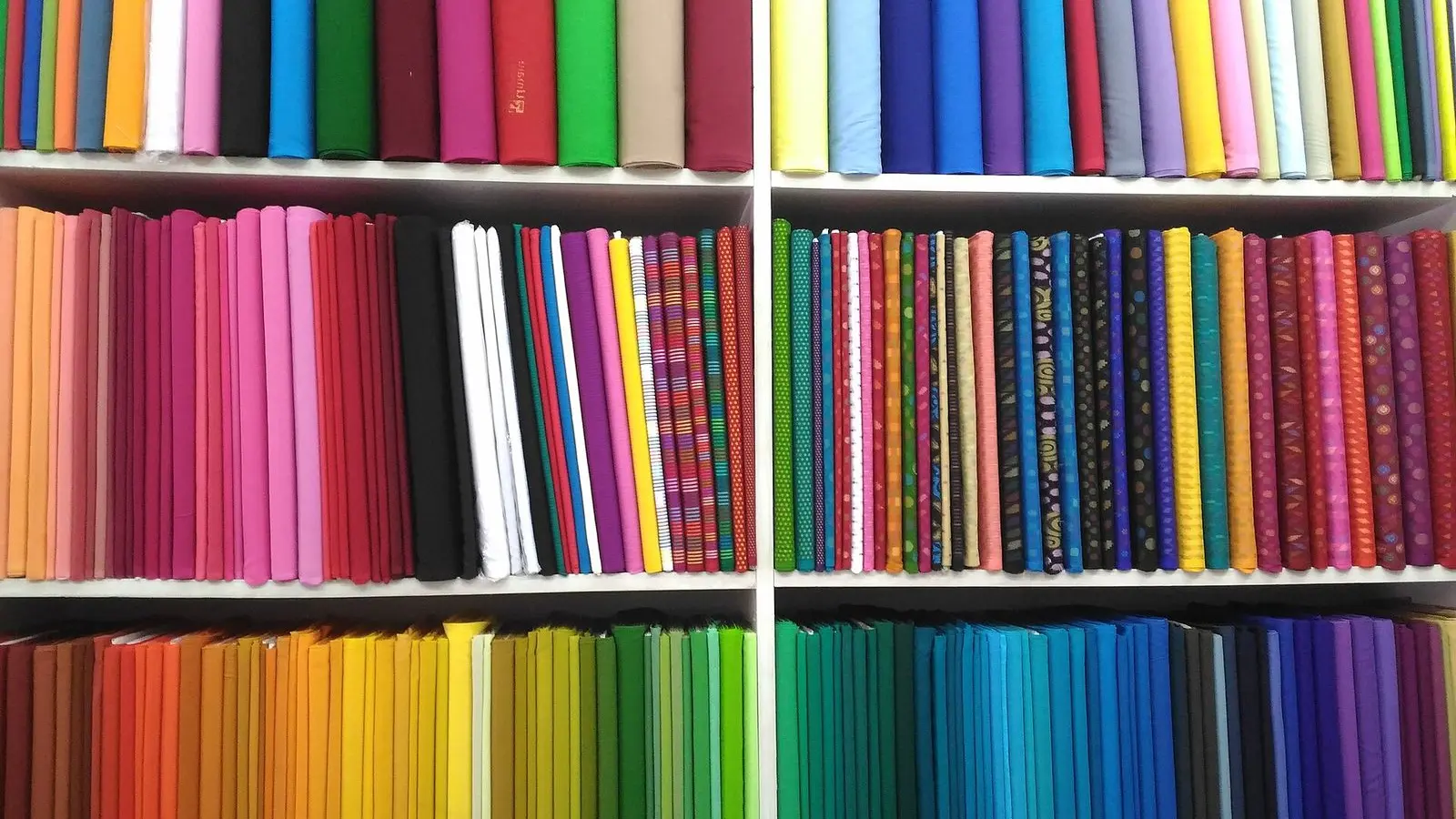Bolts of plain cloth in a rainbow of colours stacked on the shelves of a cloth shop