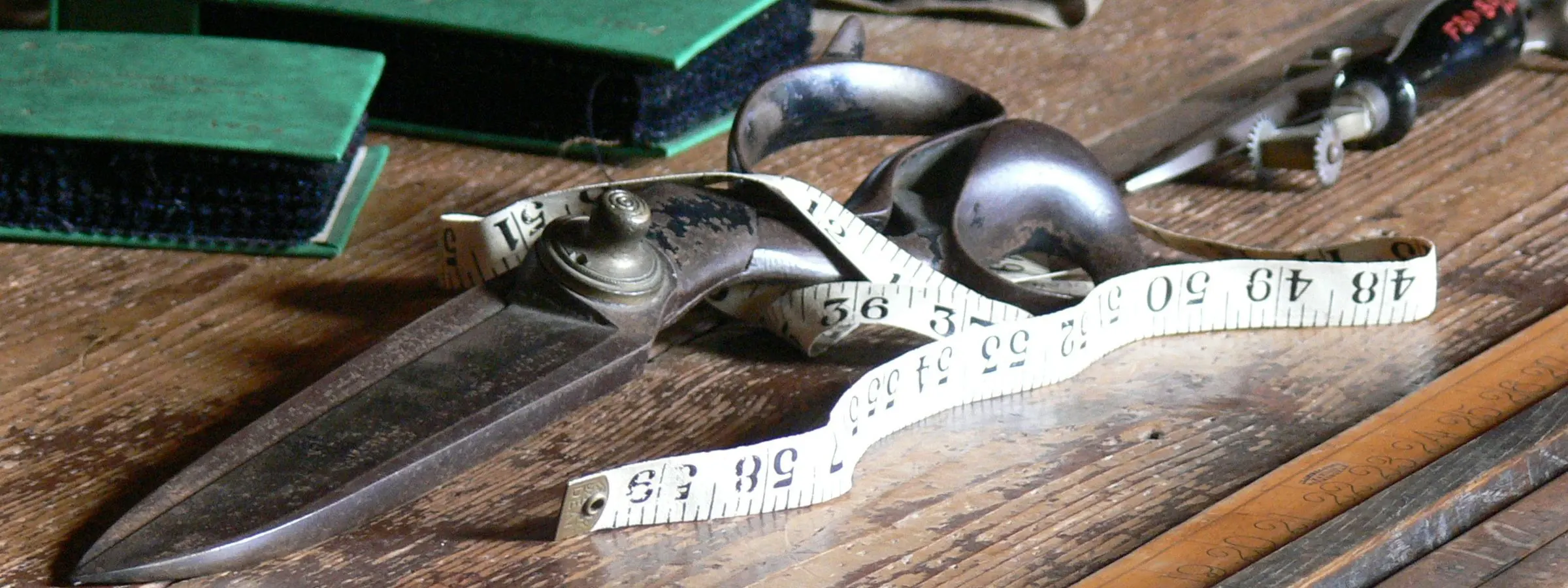 Tailor's shears, a measuring tape and cloth on a worn wooden workbench