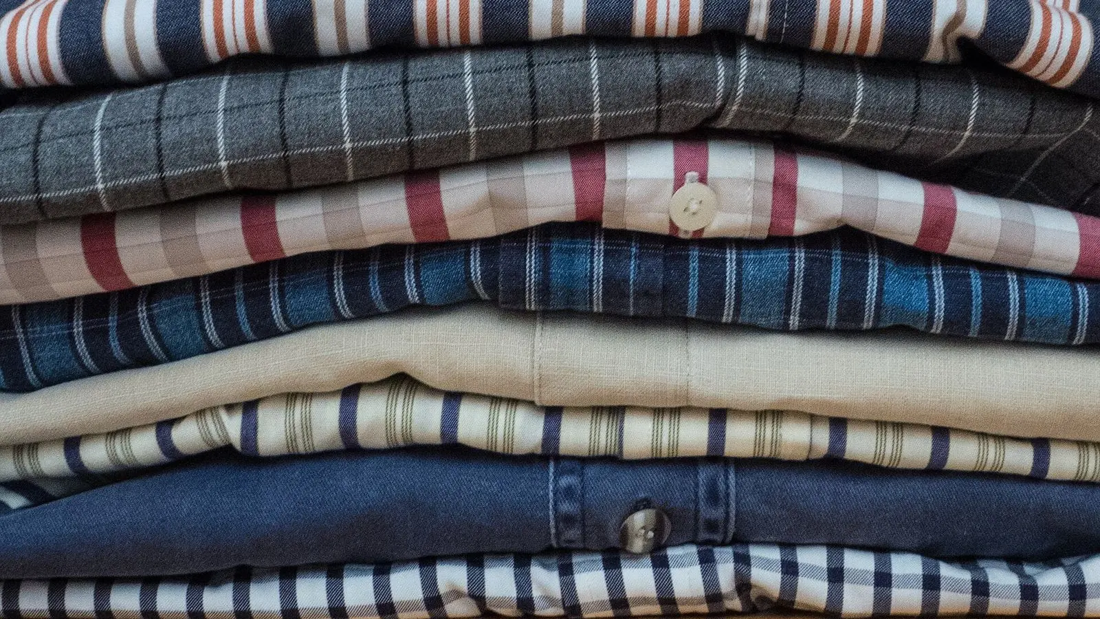 A stack of folded men's shirts in checked and striped cotton on a wooden table
